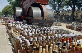 A steamroller crushing rows of discarded alcohol bottles in a public display, surrounded by trees and onlookers, symbolizing the enforcement of the Bihar alcohol ban.